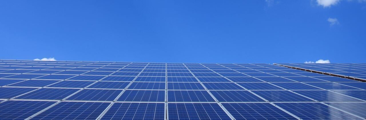 A low angle view of solar panels under a bright blue sky with clouds.